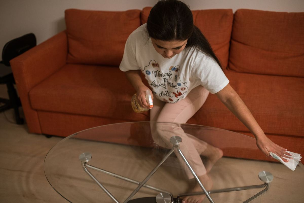 A woman wiping a glass coffee table in a living room