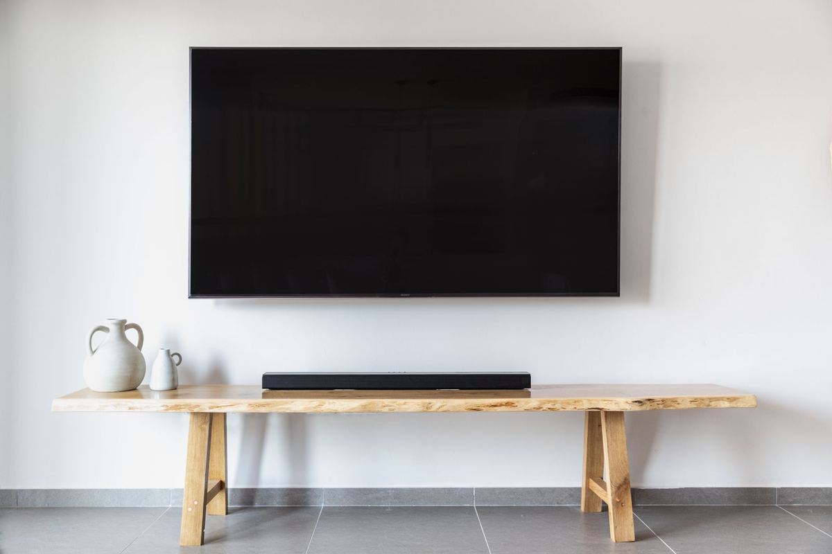 Telewizor zamontowany na ścianie nad drewnianą komodą