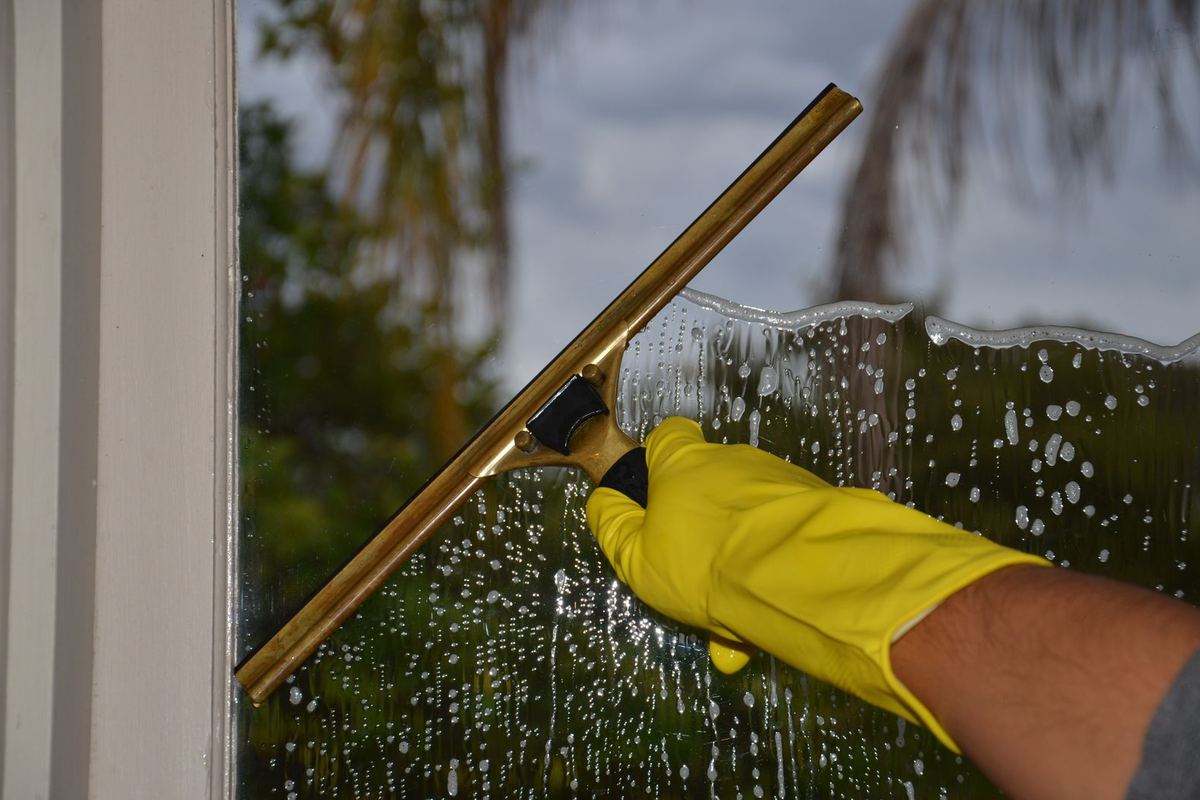 A gloved hand pulling a squeegee down a wet window pane
